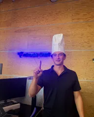 Roanin in a chef hat holding up one finger in front of the Avoca West sign