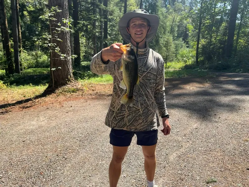 Roanin in a bucket hat holding a largemouth bass