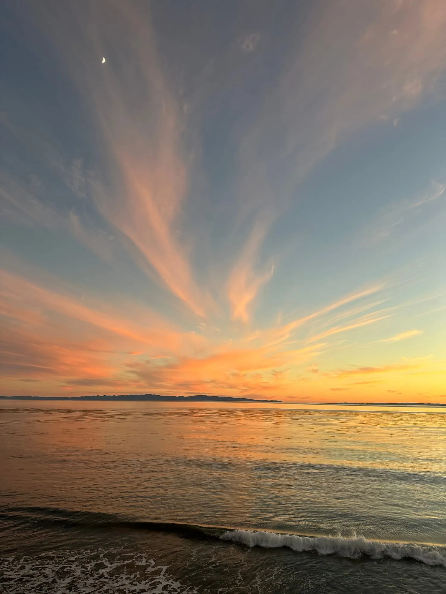 A sunset over the ocean off Santa Barbara, a sliver of moon above the clouds